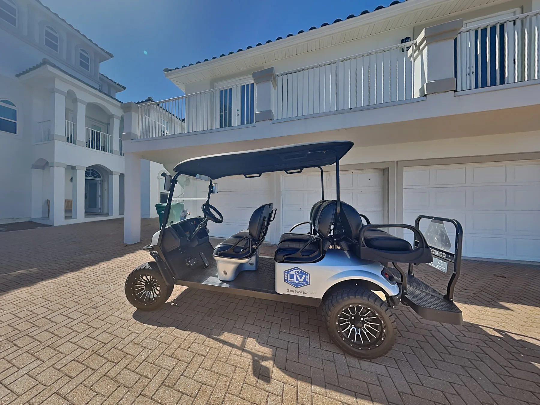 A golf cart is parked on a paved driveway in front of a large white house.