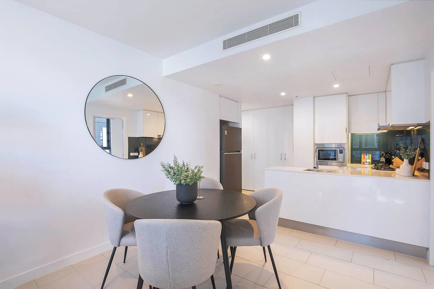 A dining area with a round table and cushioned seating beside an open kitchen.