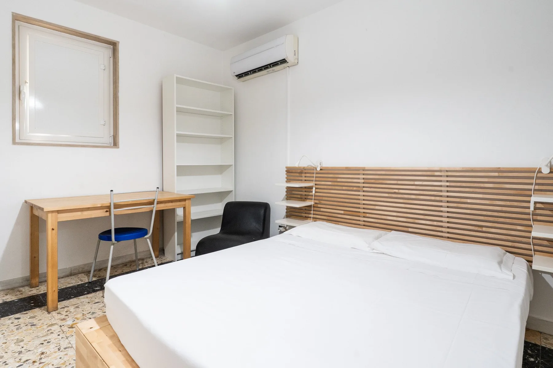 A bedroom with a bed, a desk, and a wall-mounted air conditioner.