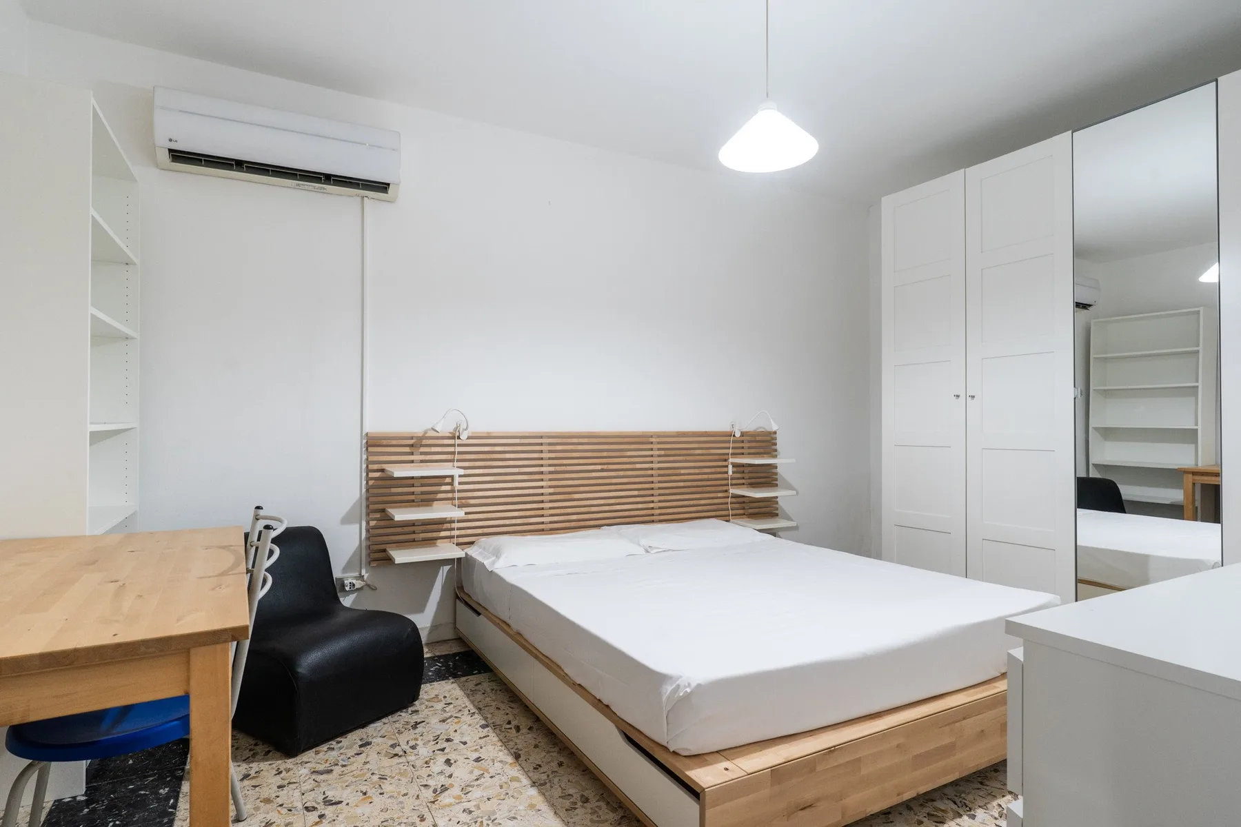 A bright bedroom with a bed, wooden desk, and white wardrobe.