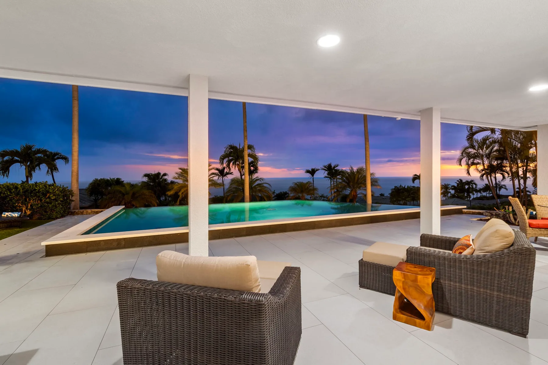 Un patio cubierto da a una piscina y palmeras al anochecer.