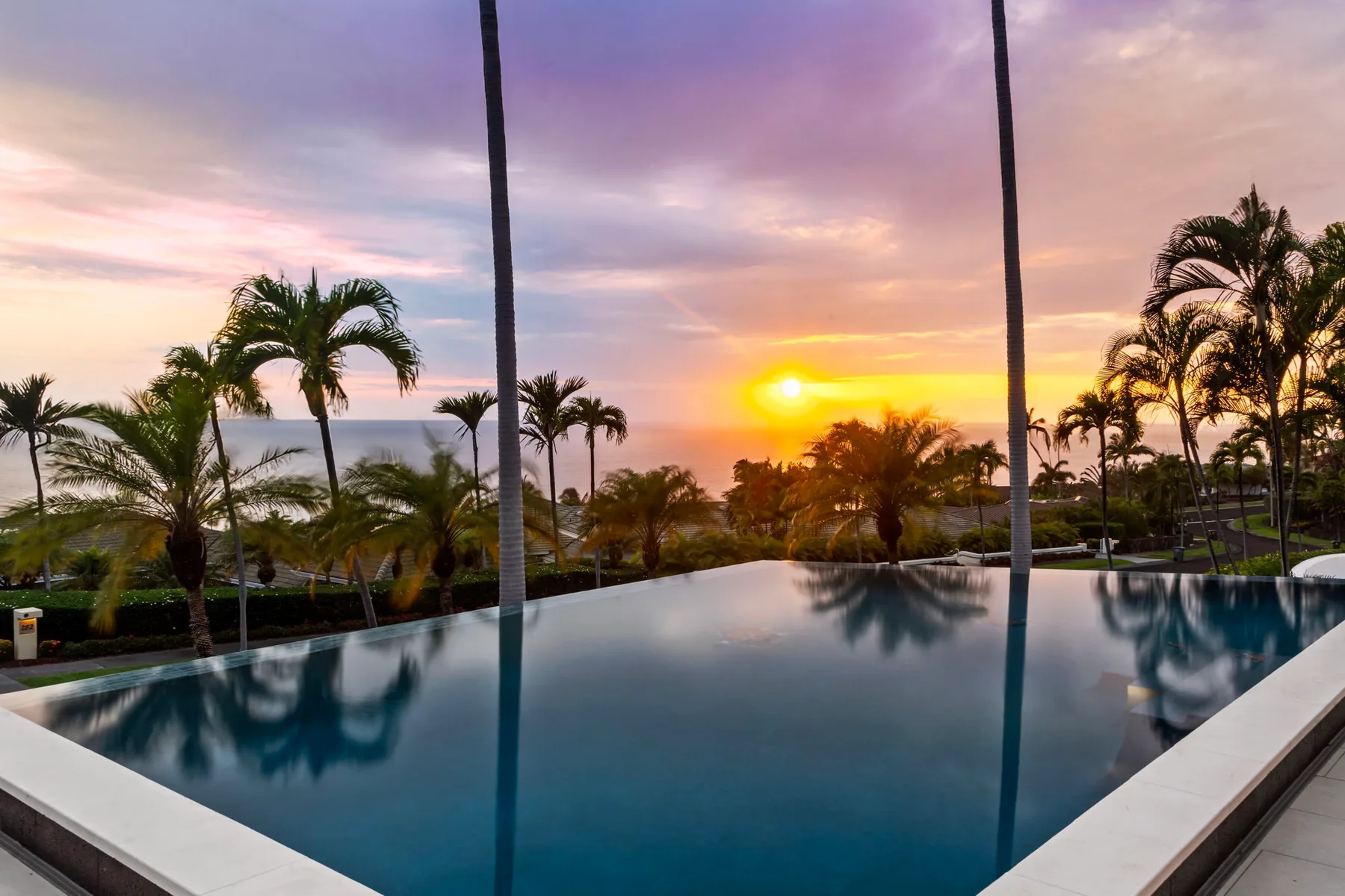 Una piscina al aire libre refleja palmeras bajo un cielo de atardecer colorido.