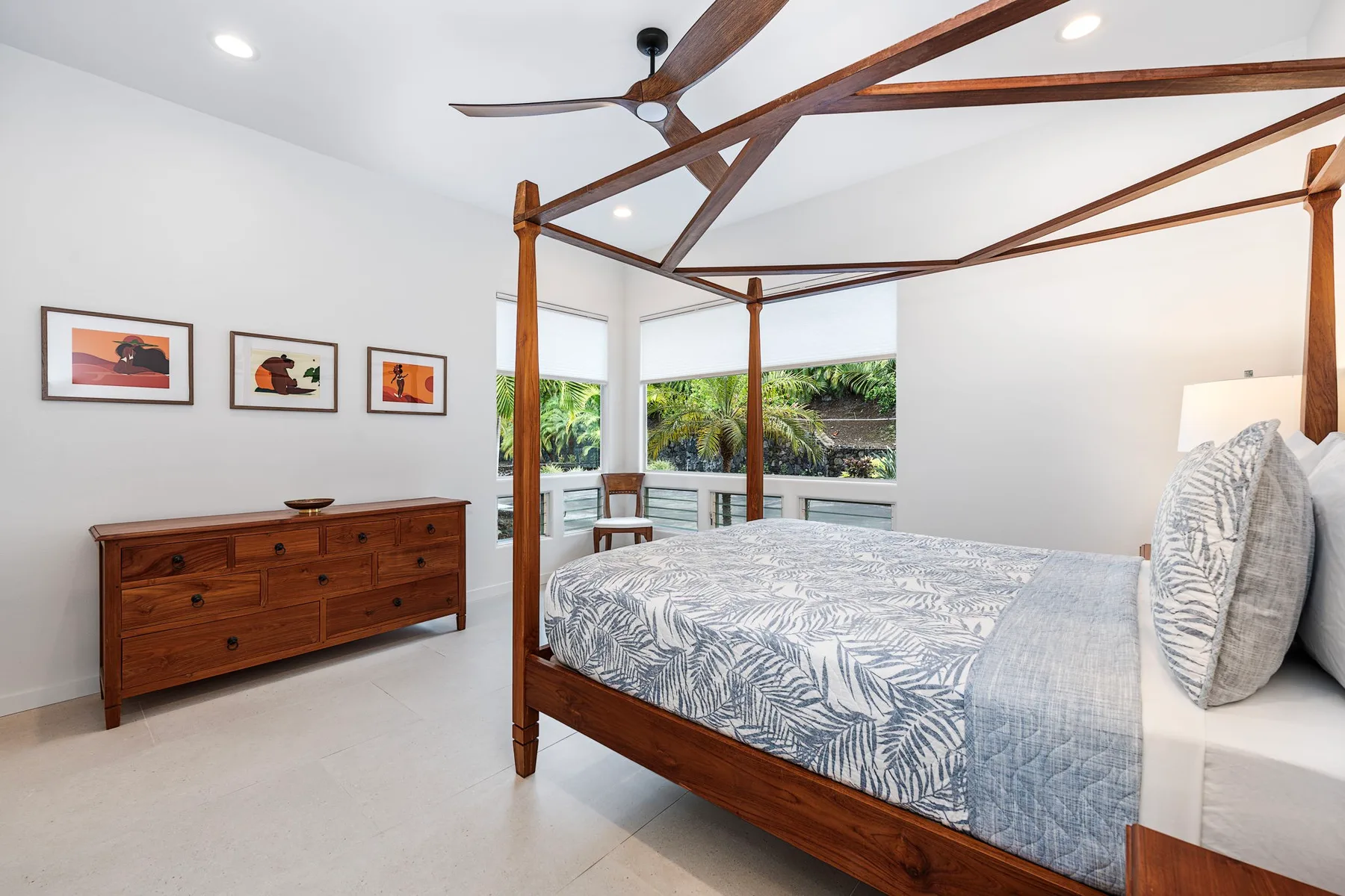 Un dormitorio luminoso con cama de madera, ropa de cama estampada y ventanas con vistas a la vegetación.