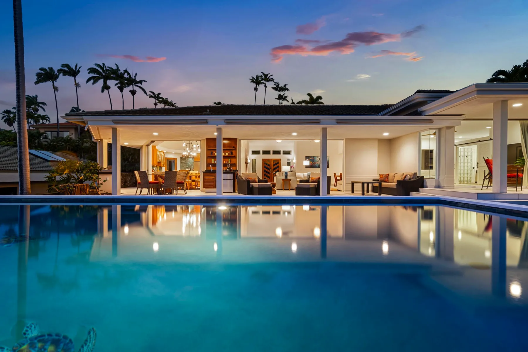 Una casa moderna con patio iluminado da a una piscina al anochecer.