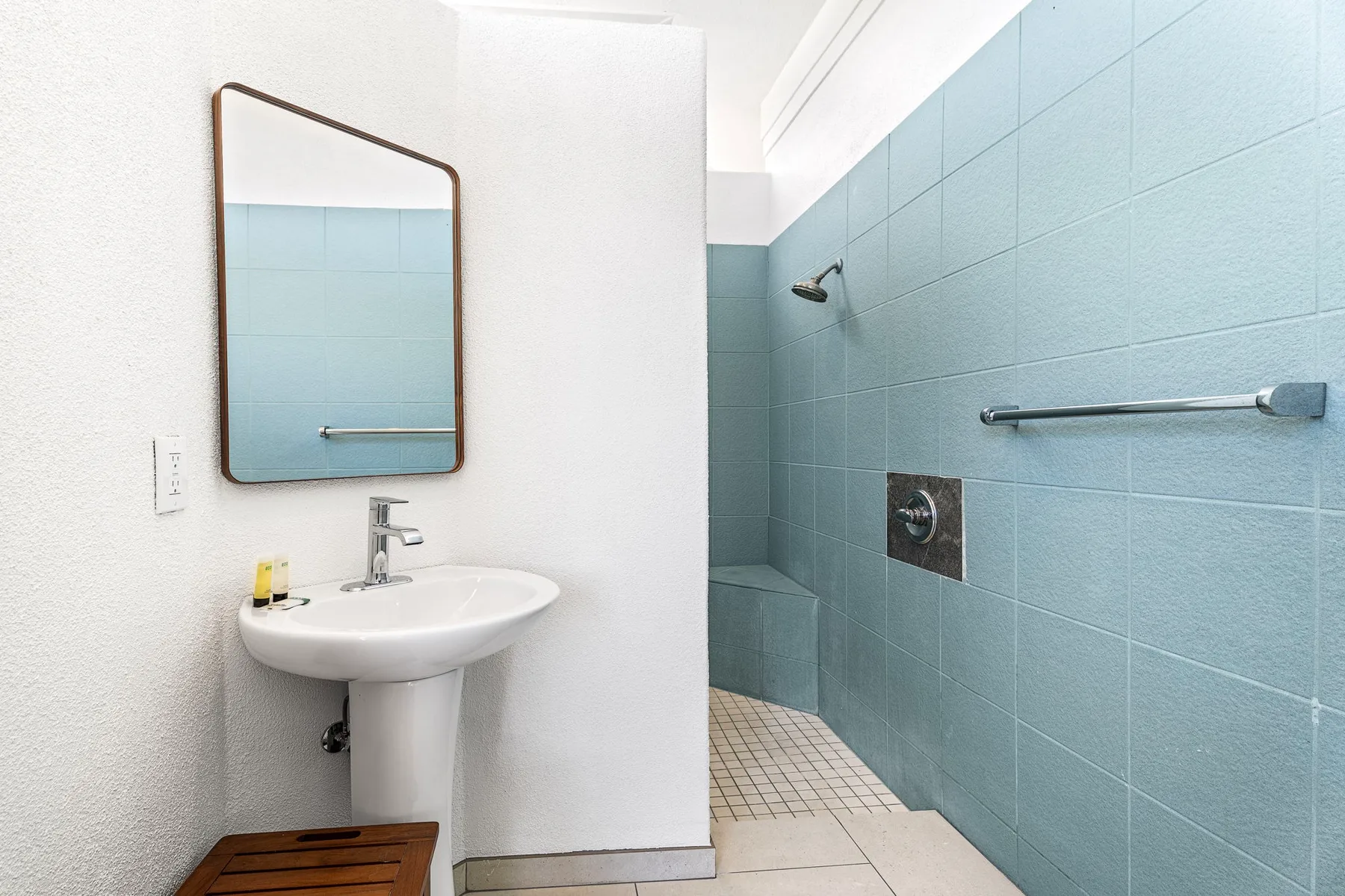 Un baño con lavabo de pedestal, espejo y zona de ducha con azulejos.