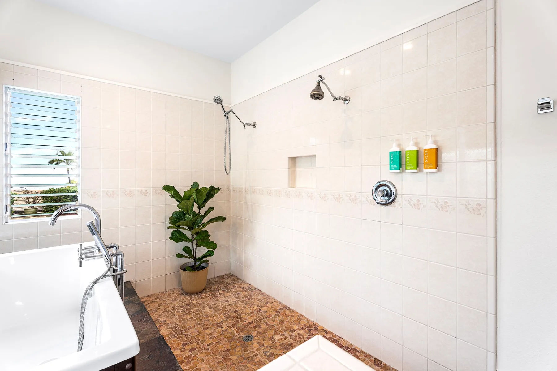 Un baño alicatado con bañera, accesorios de ducha y una planta en maceta.