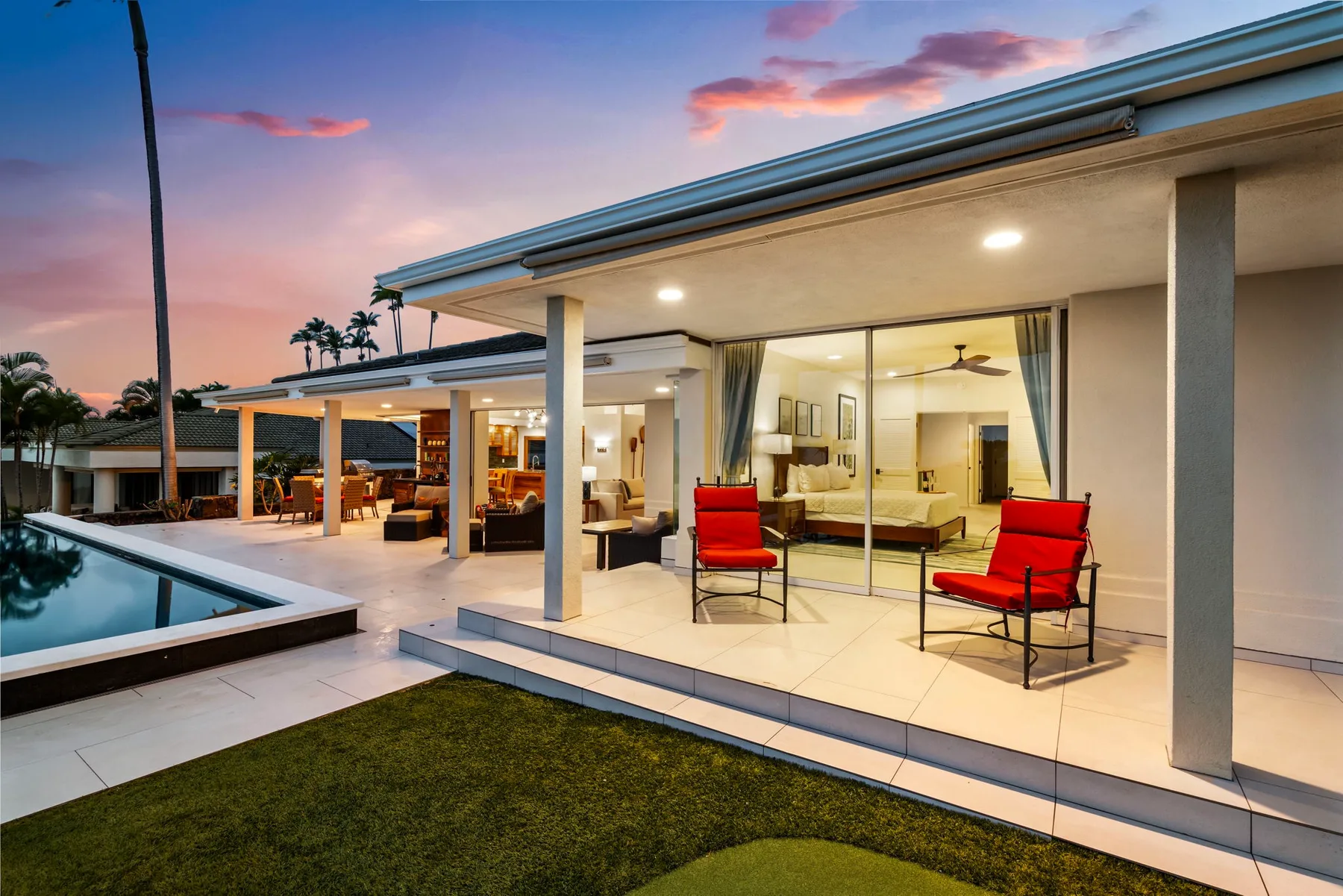 Un patio moderno con asientos rojos da a una piscina al anochecer.