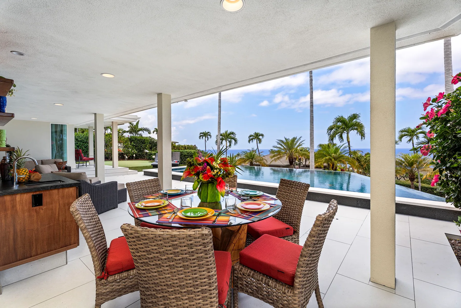 Un comedor exterior cubierto tiene vistas a una piscina y palmeras.