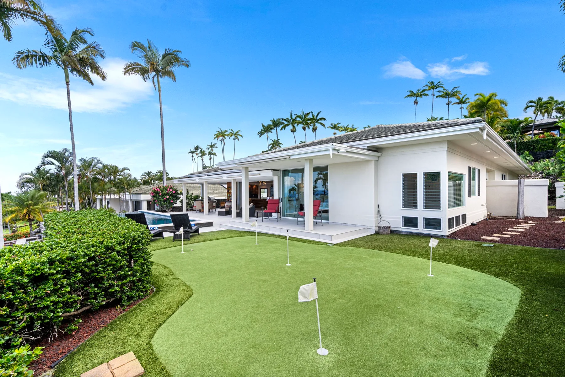 Una casa moderna da a un pequeño putting green, con palmeras en el jardín.