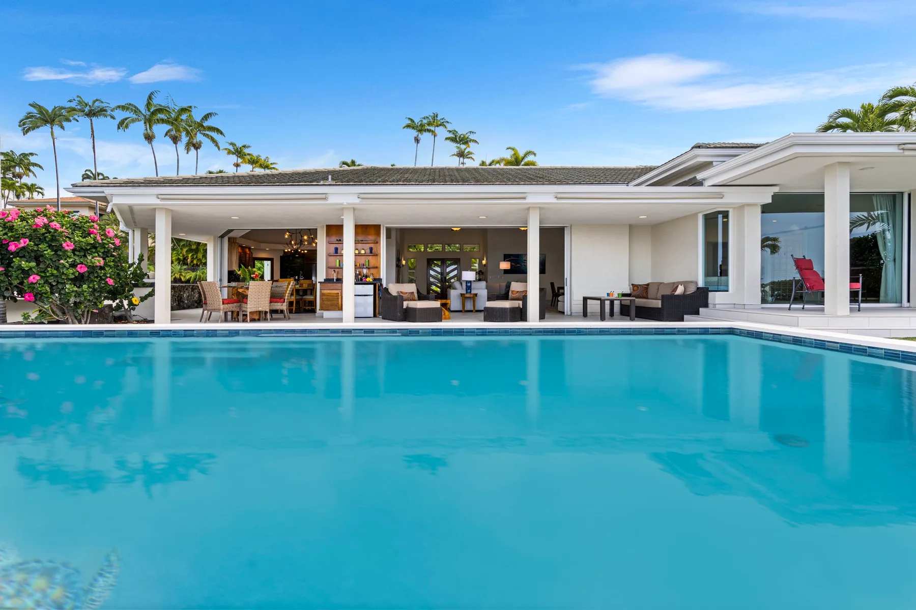 Una piscina frente a una casa moderna con una zona de estar abierta.