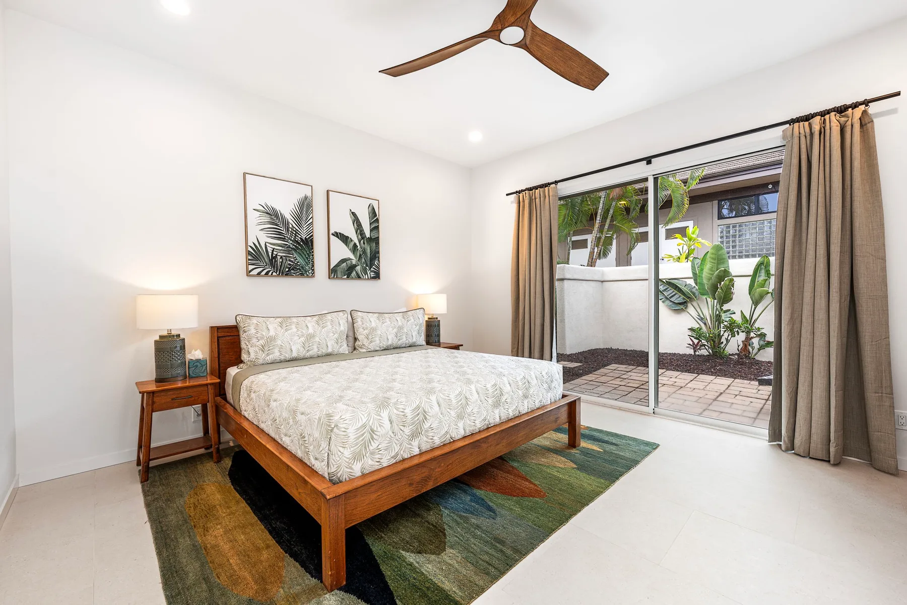 Un dormitorio luminoso con una cama de madera y puertas corredizas de vidrio hacia un patio.