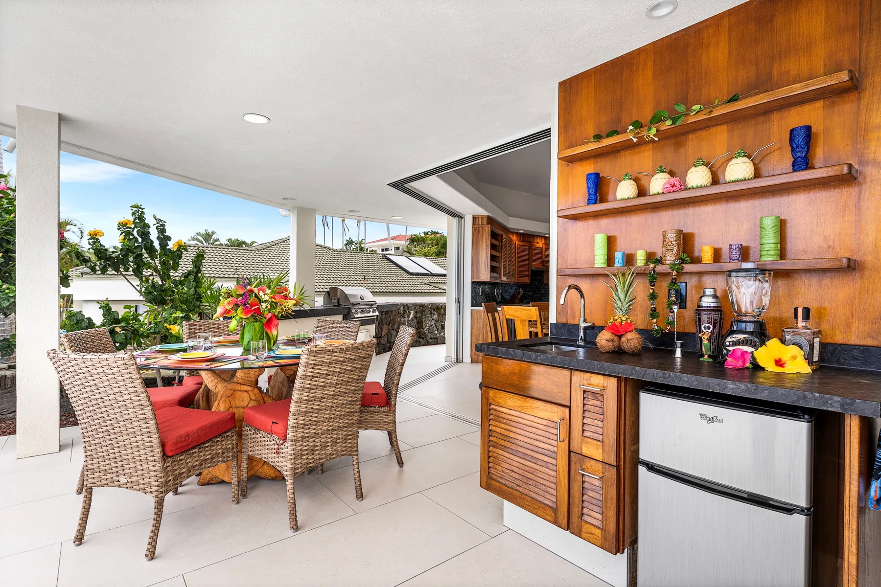 Comedor exterior cubierto junto a una barra de madera con un refrigerador pequeño.