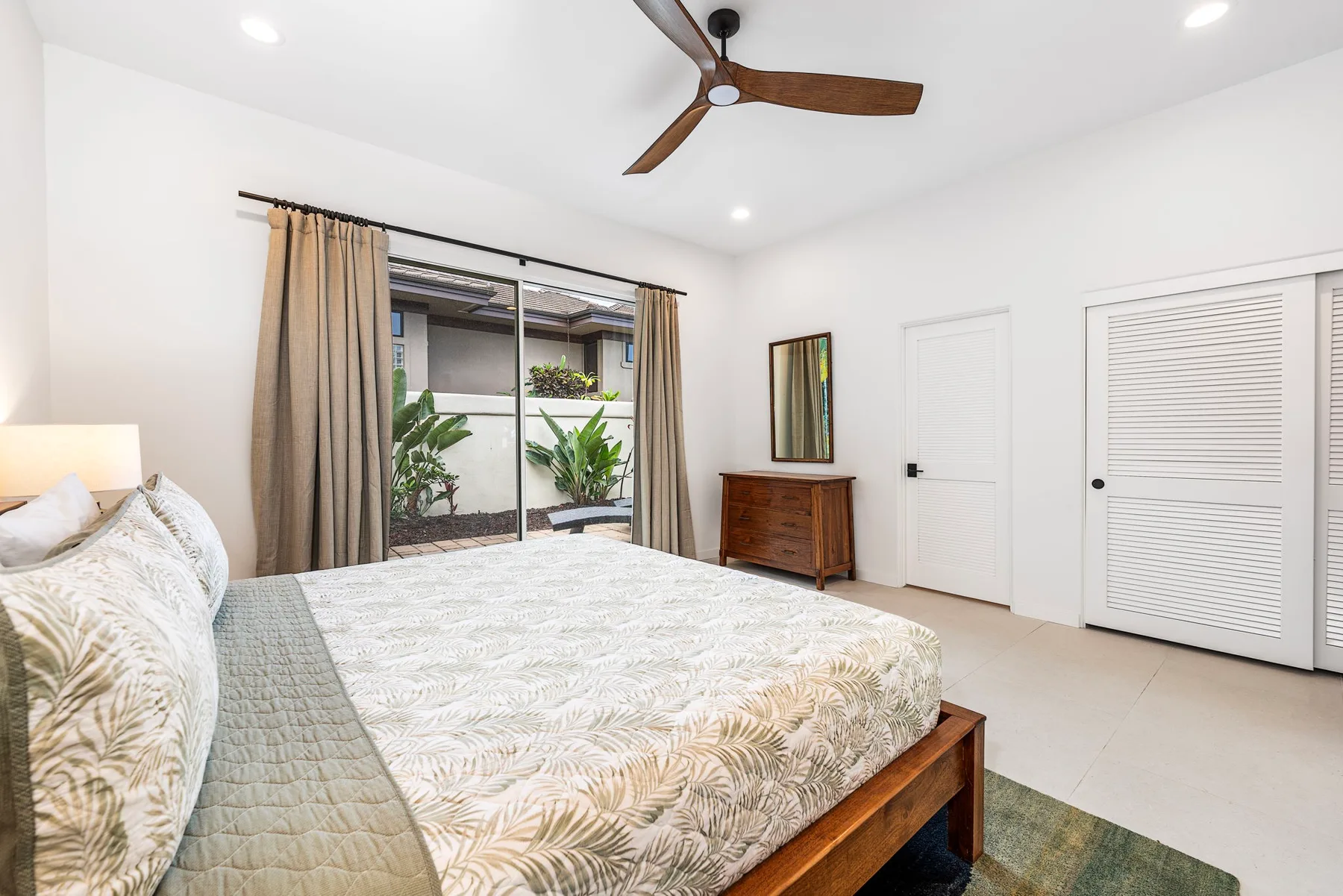 Un dormitorio luminoso con una cama junto a una ventana grande con cortinas.