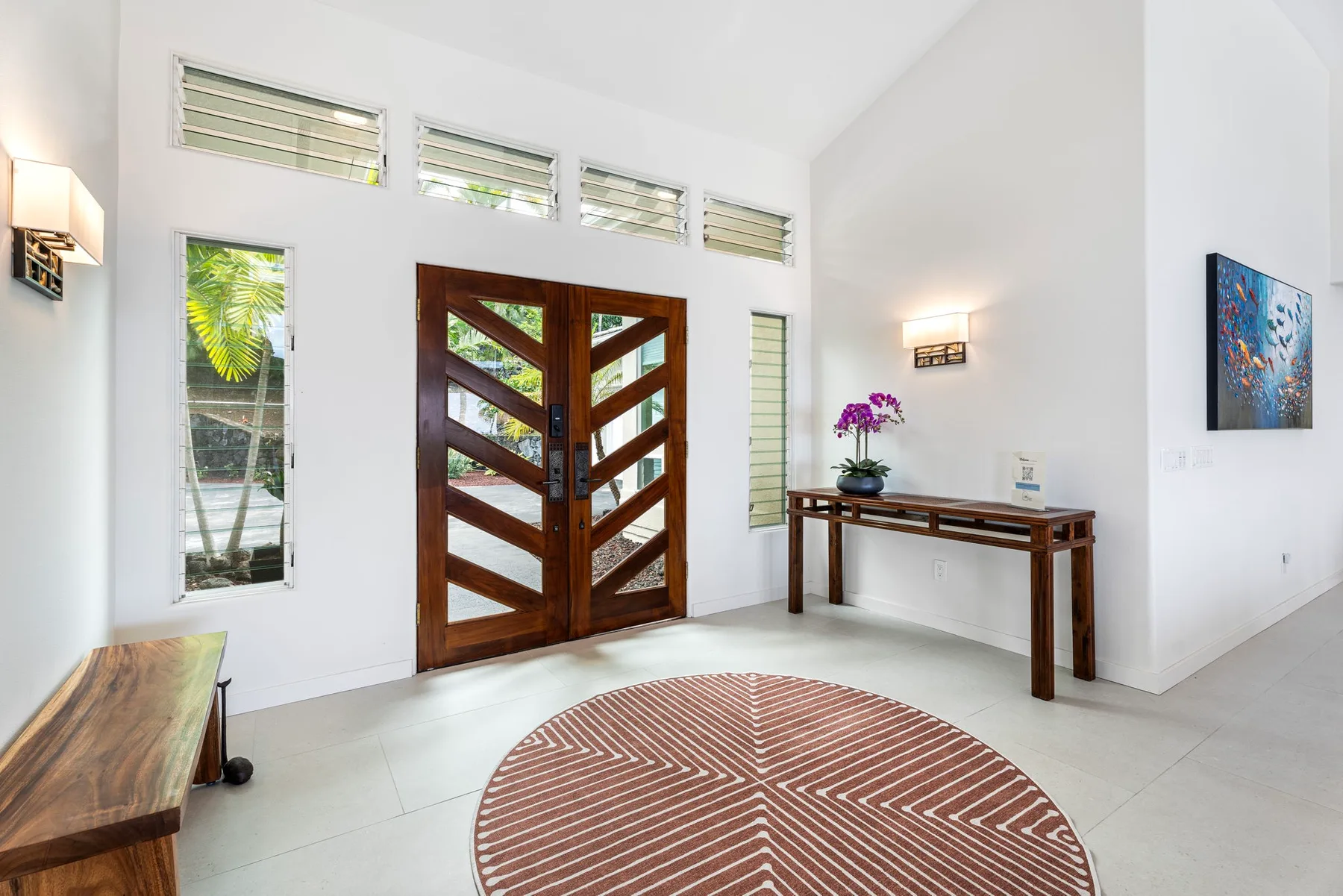 Una entrada luminosa tiene una puerta doble de madera y una alfombra redonda estampada.
