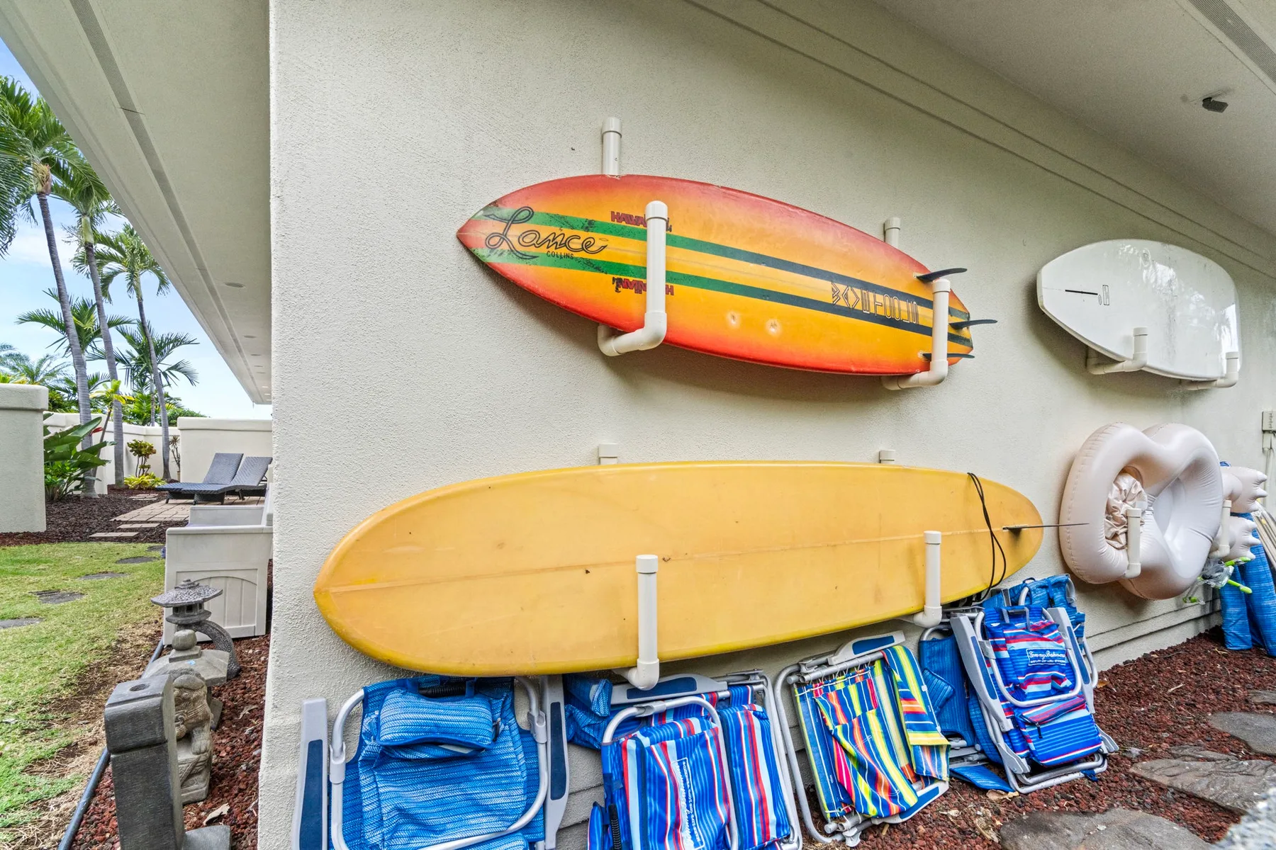 Pared exterior con tablas de surf de colores sobre sillas de playa y otros artículos.