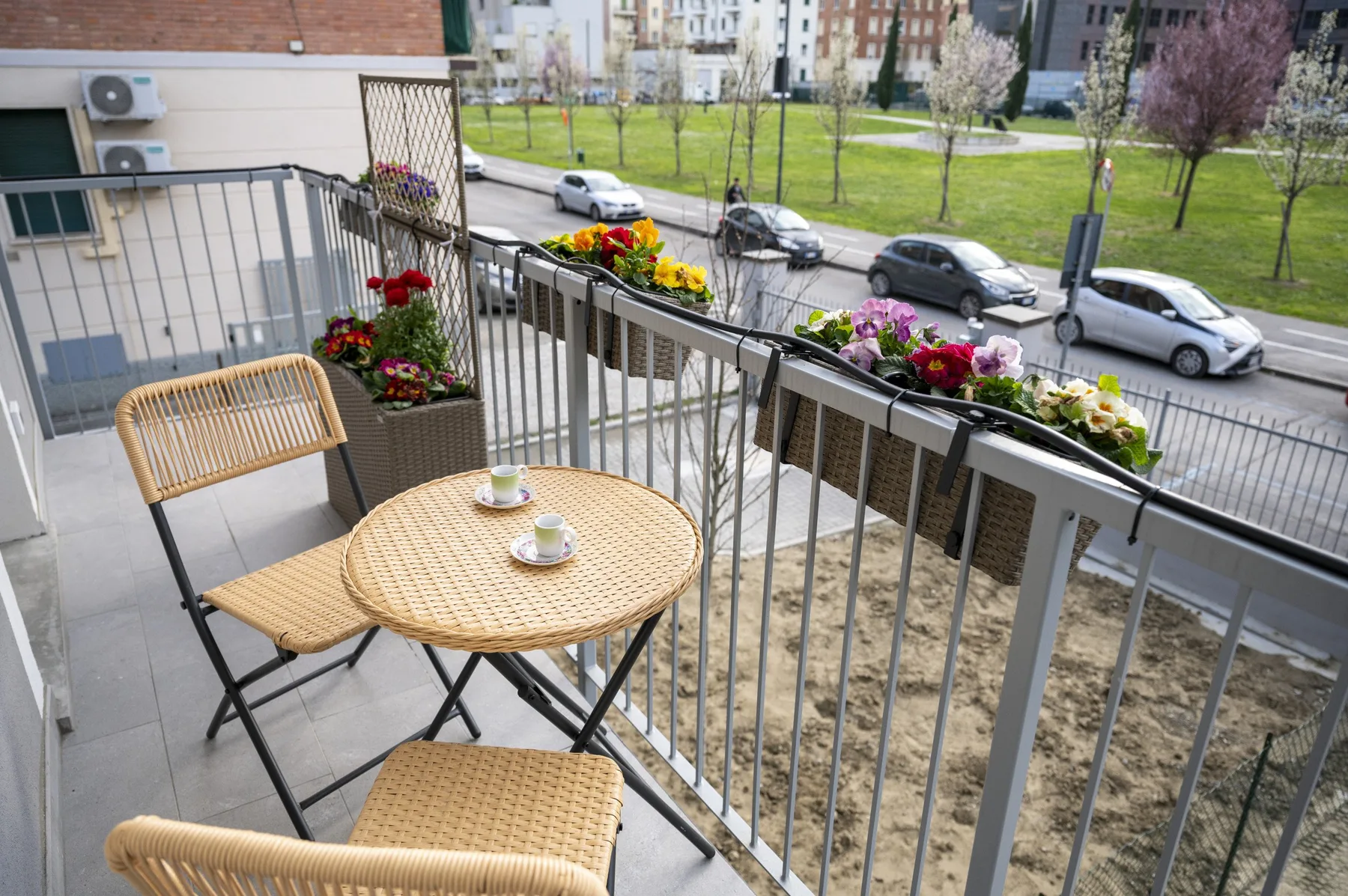 Una zona de estar en un balcón con una mesa redonda y jardineras de flores da a una calle.