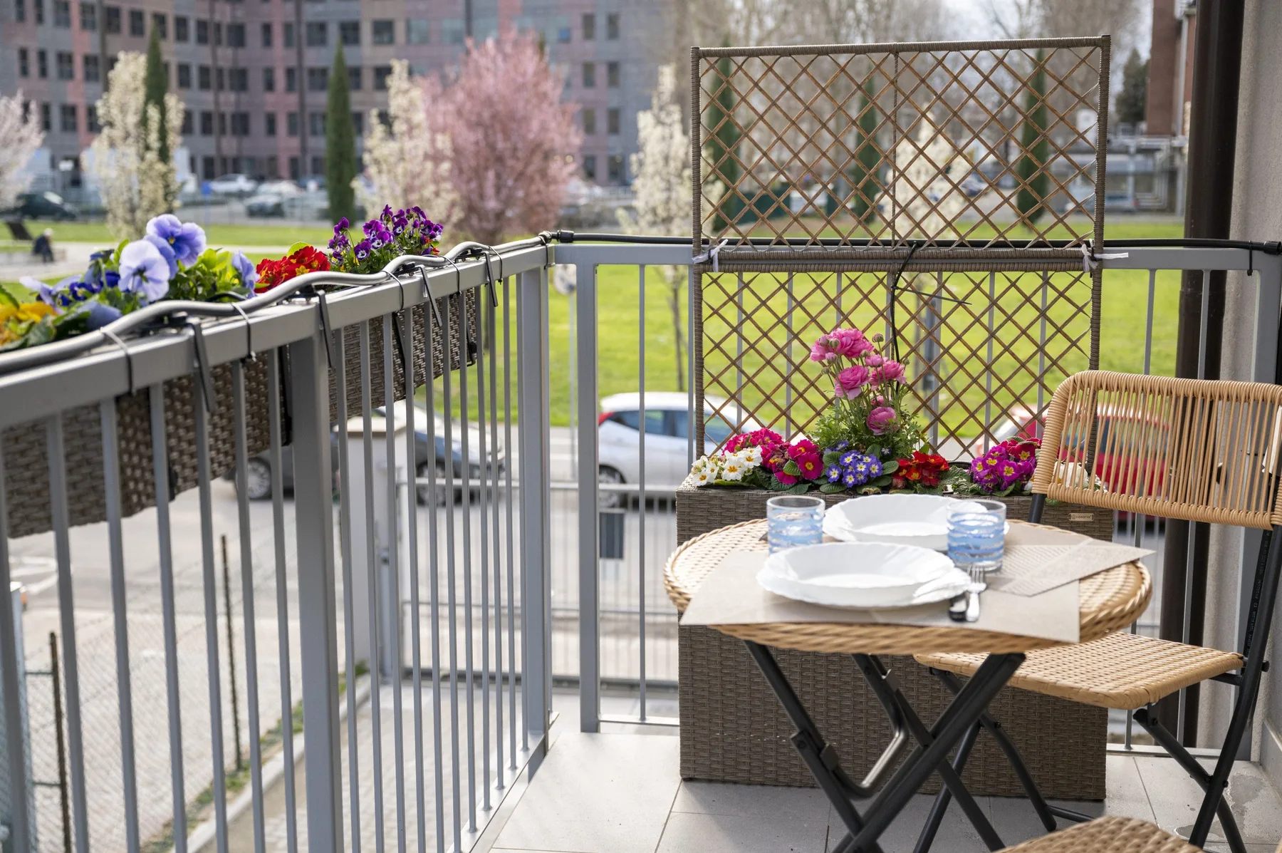 Comedor de balcón con una mesa pequeña, sillas y jardineras con flores.