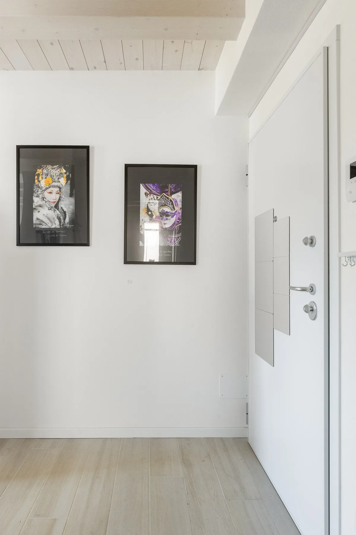 Una entrada luminosa con cuadros en la pared junto a una puerta blanca.