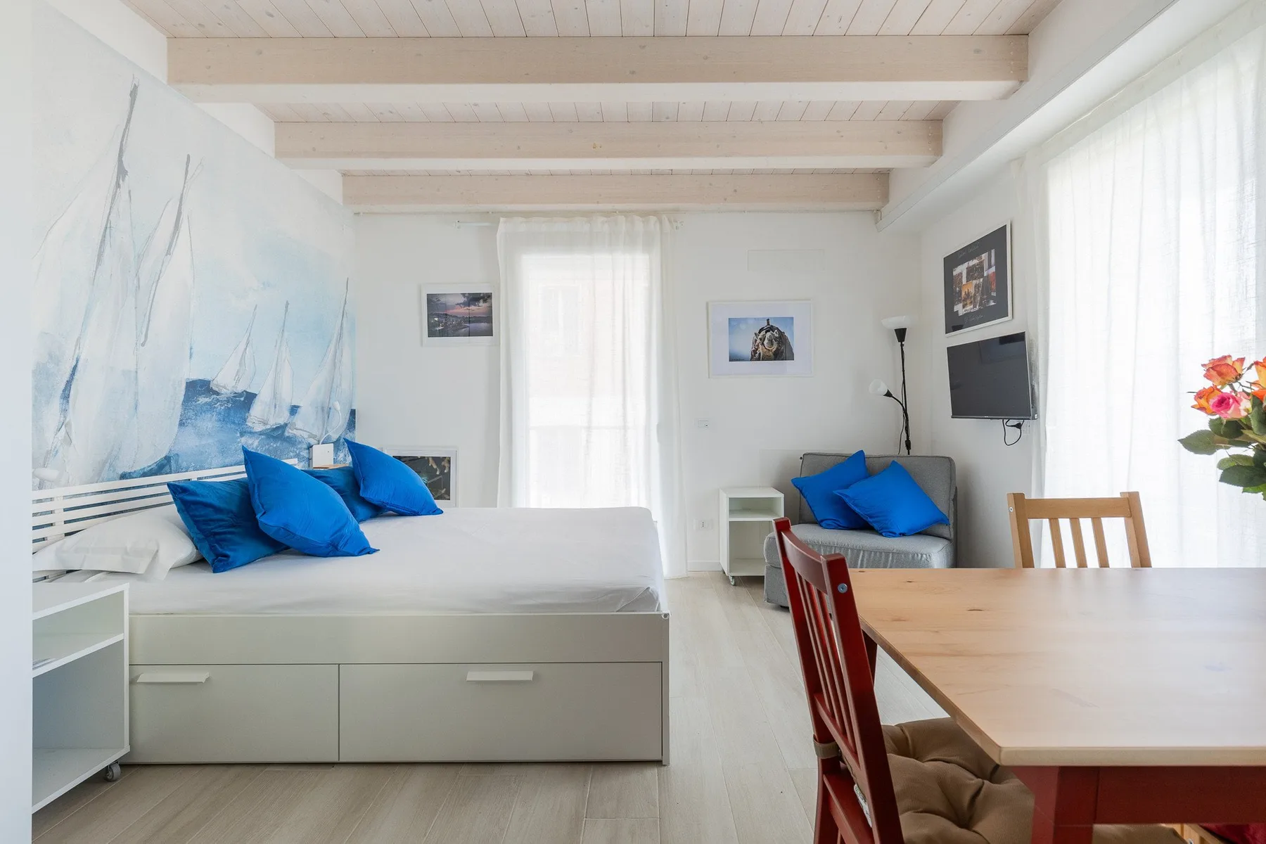 Un dormitorio luminoso con una cama, una pequeña zona de estar y una mesa de comedor.