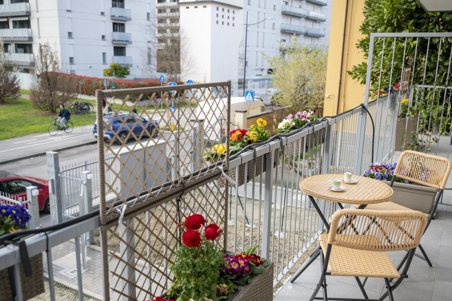 Una zona de estar en un balcón da a una calle, con flores junto a la barandilla.