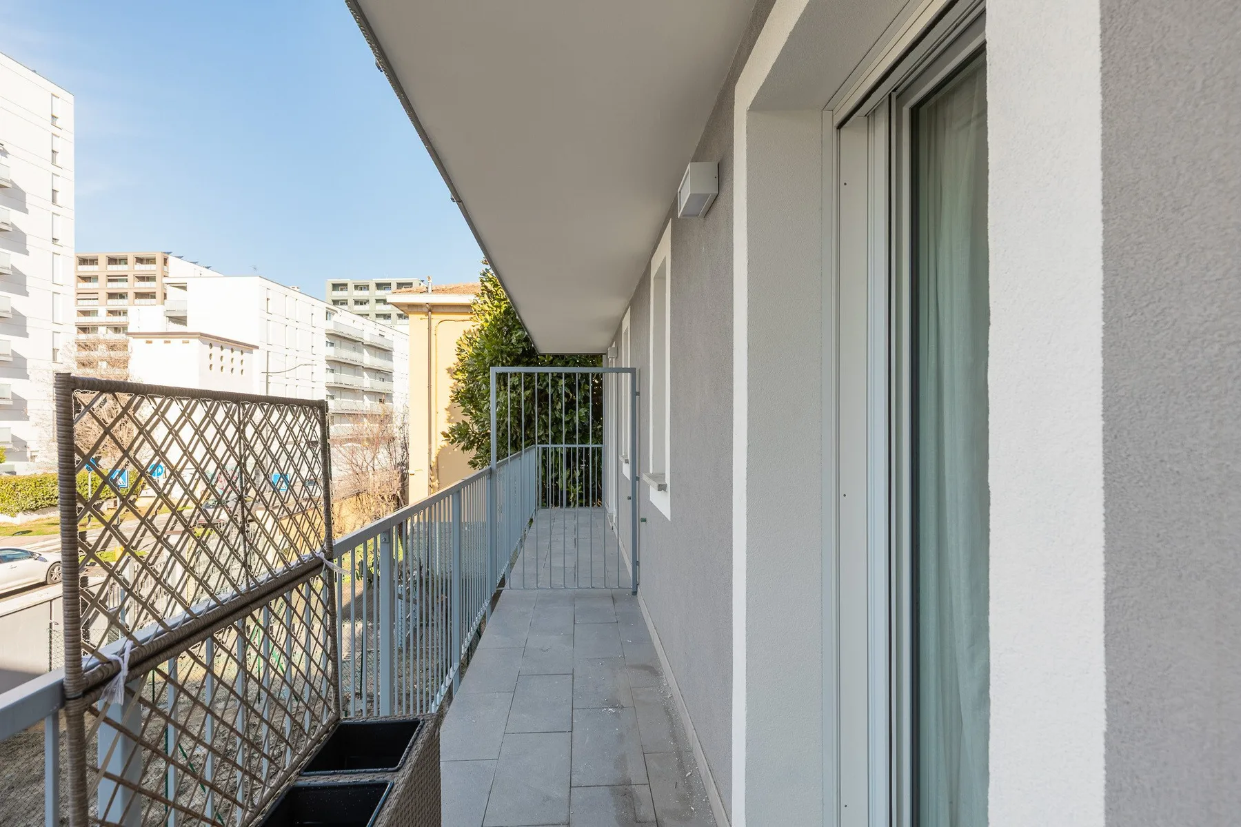 Un balcón estrecho con barandilla metálica da a edificios de apartamentos cercanos.