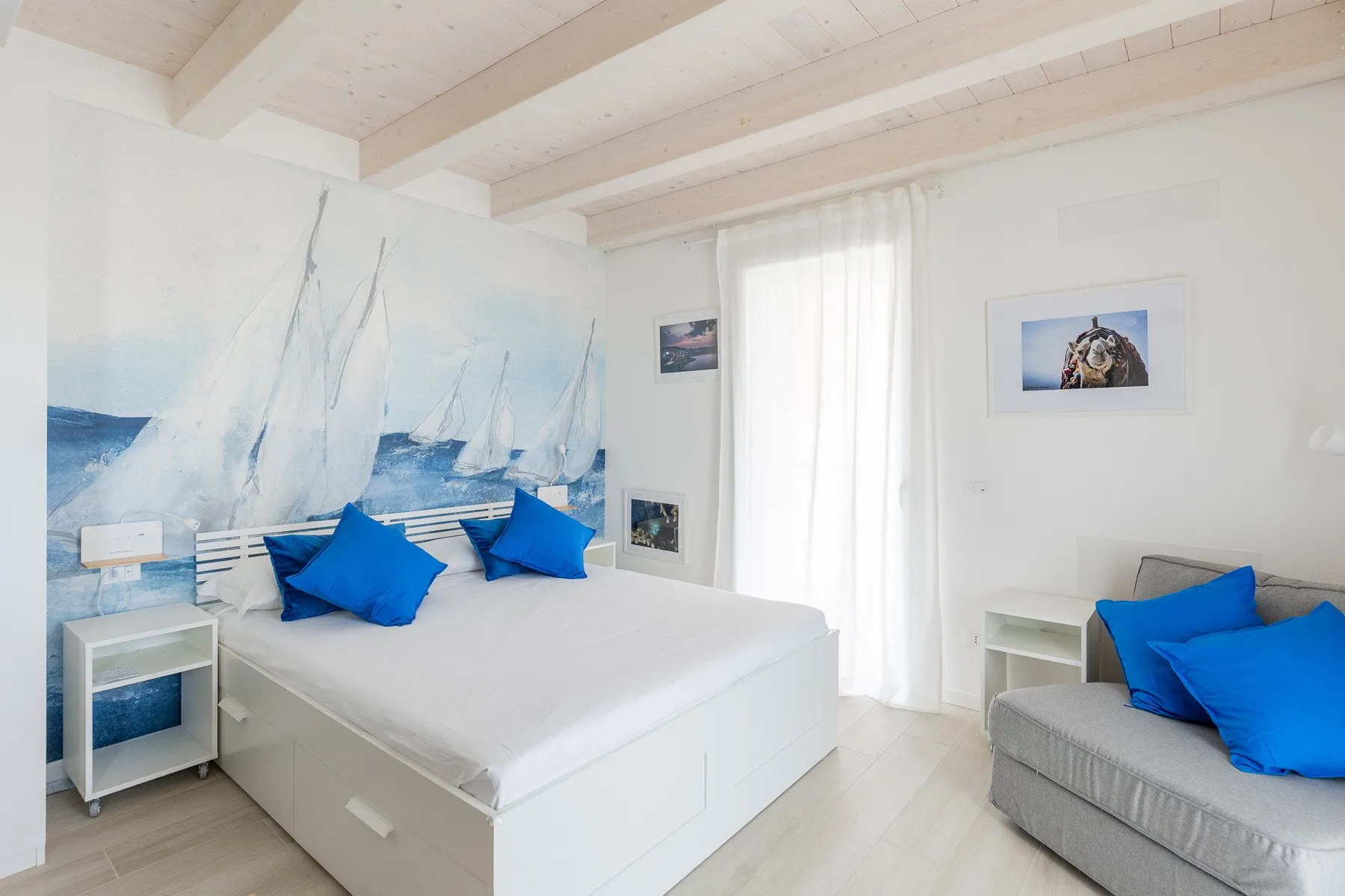 Un dormitorio luminoso con una cama, ropa de cama azul y un mural de veleros.