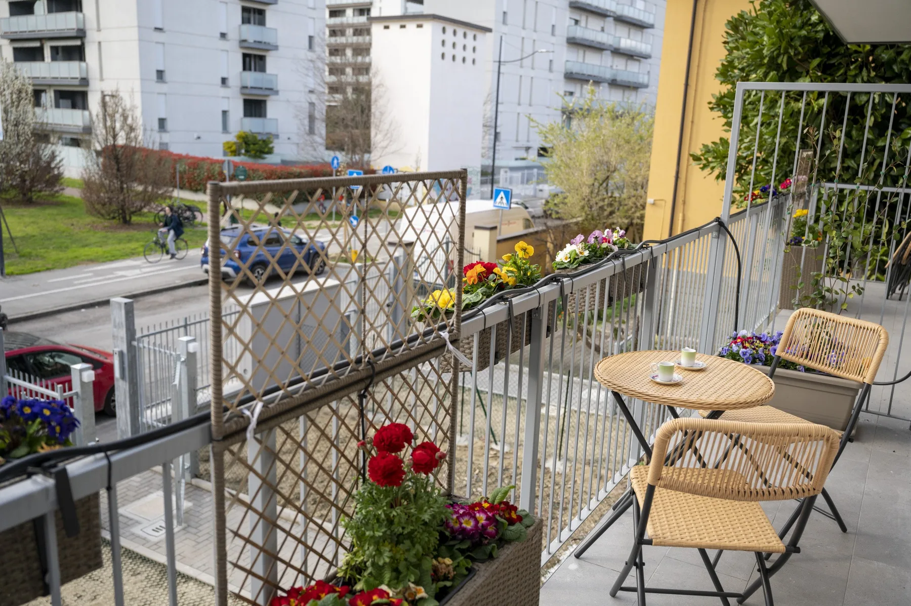Un balcón con asientos y jardineras con flores da a una calle residencial.