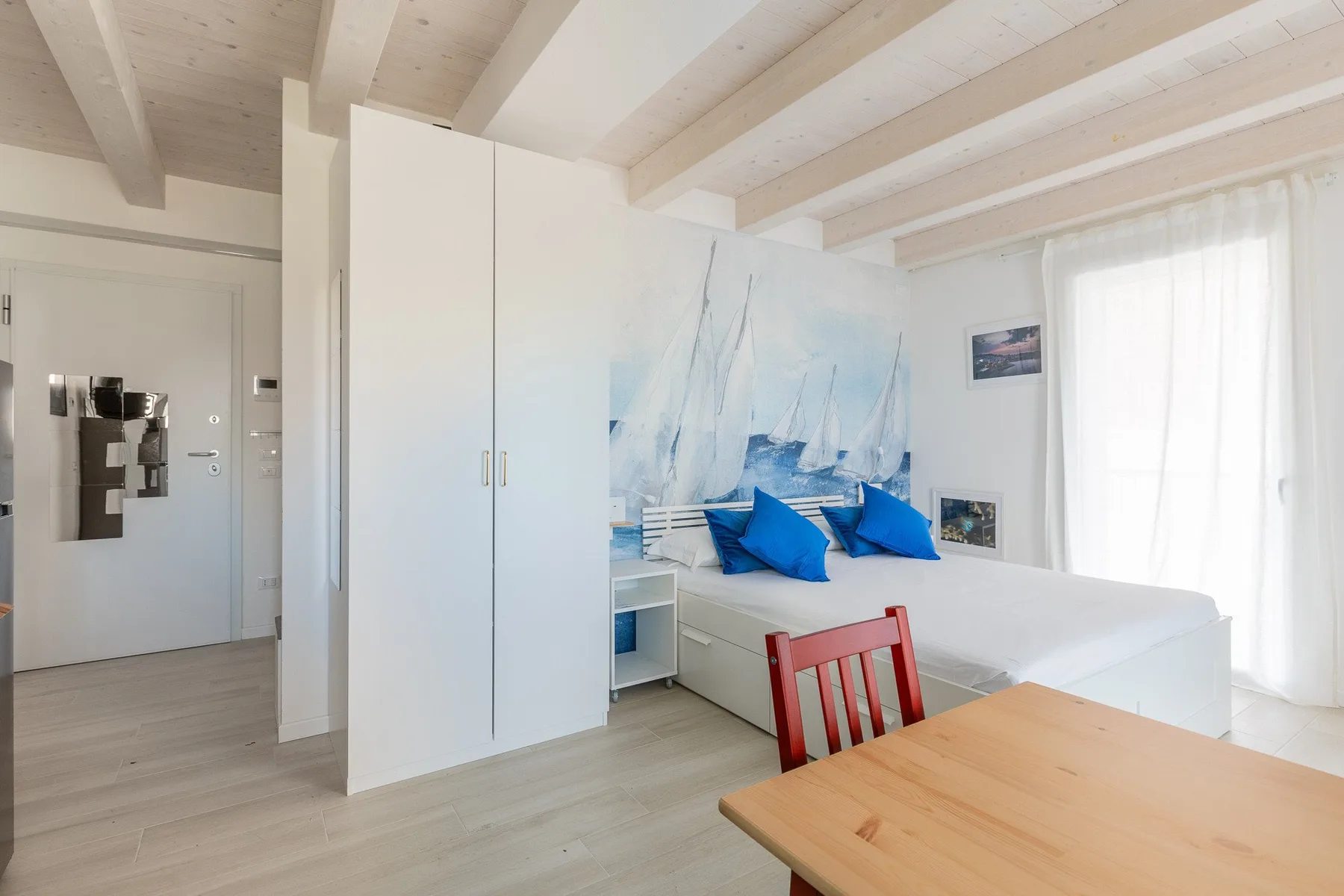 Un dormitorio luminoso con una cama bajo un mural de veleros y una mesa en primer plano.