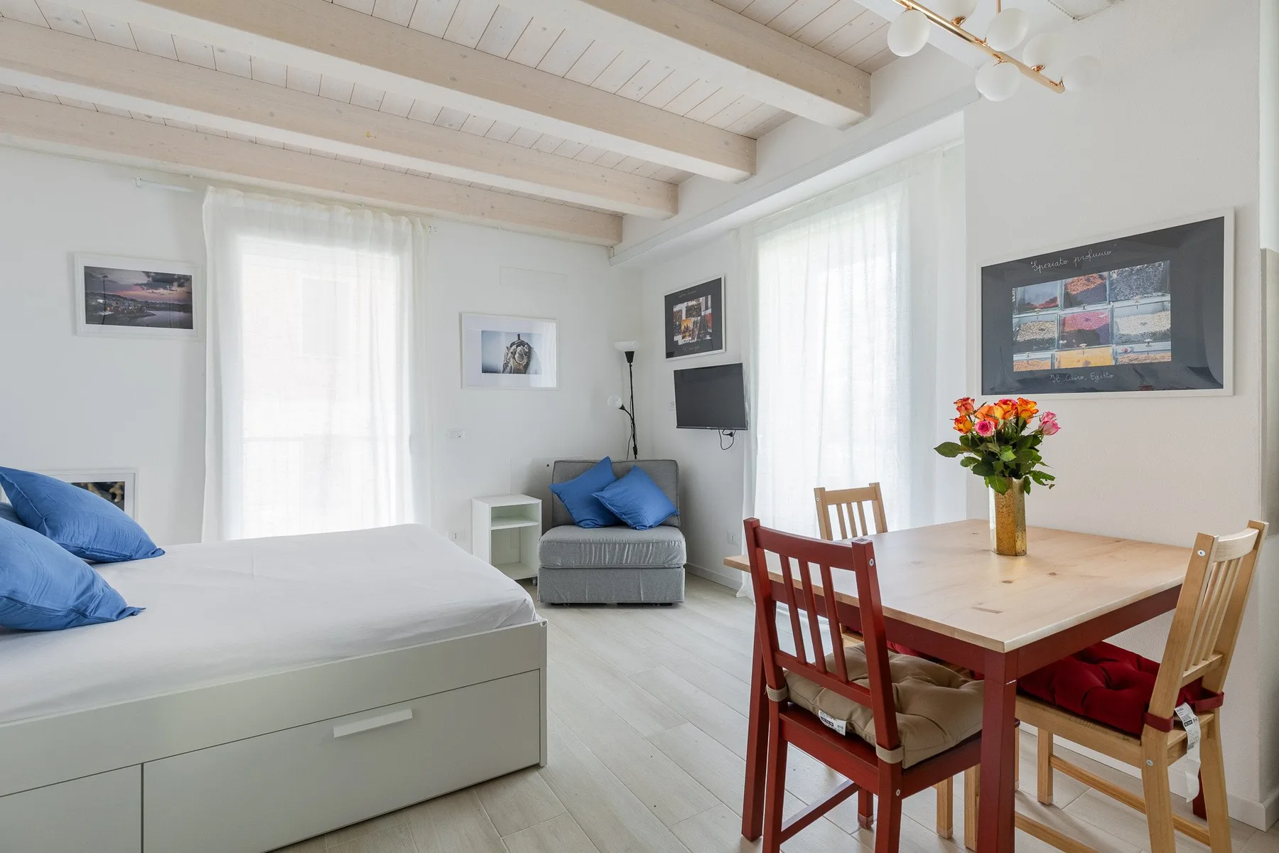 Un dormitorio luminoso con una cama, una pequeña zona de estar y una mesa de comedor.