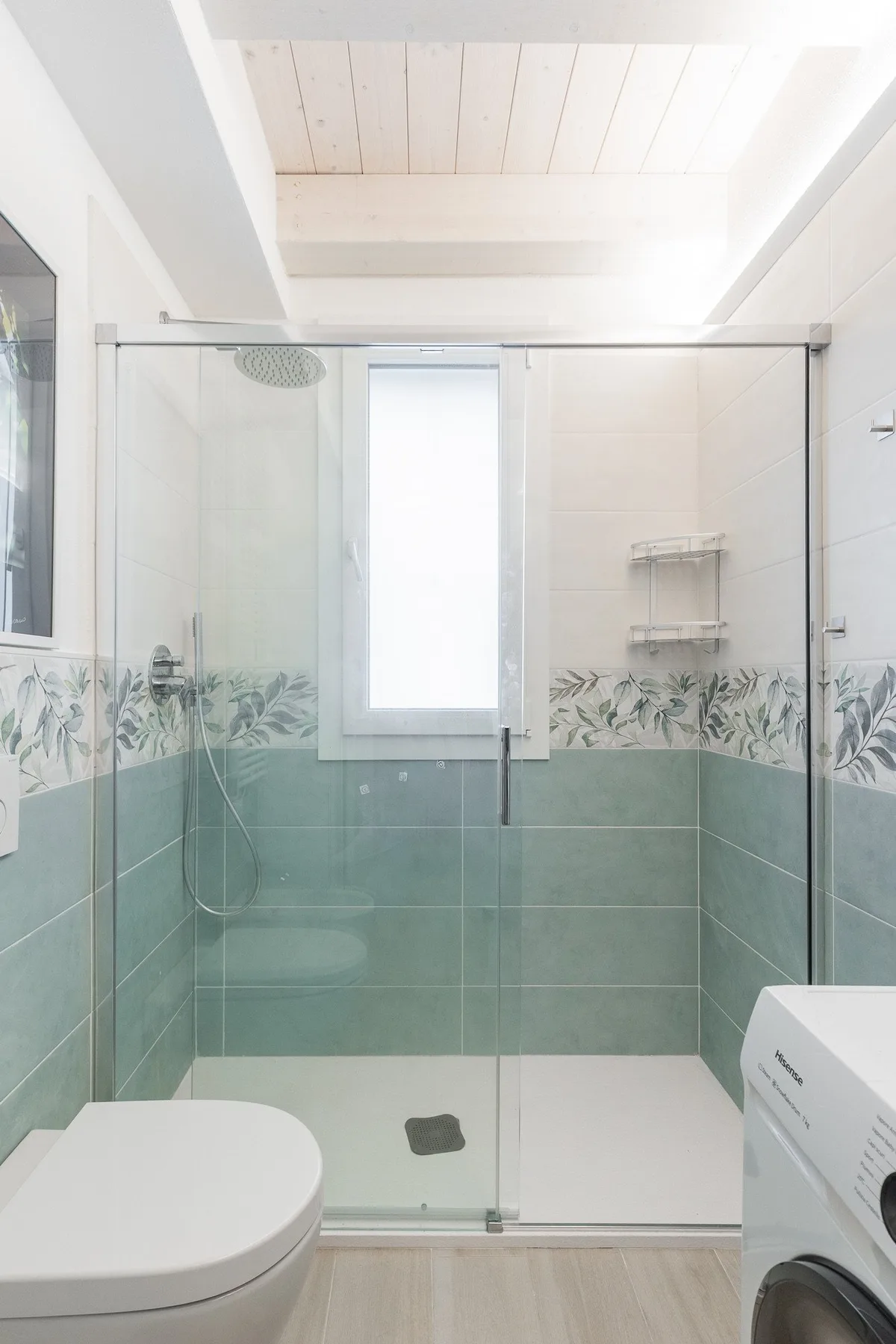 Un baño luminoso con ducha de cristal, inodoro y lavadora.
