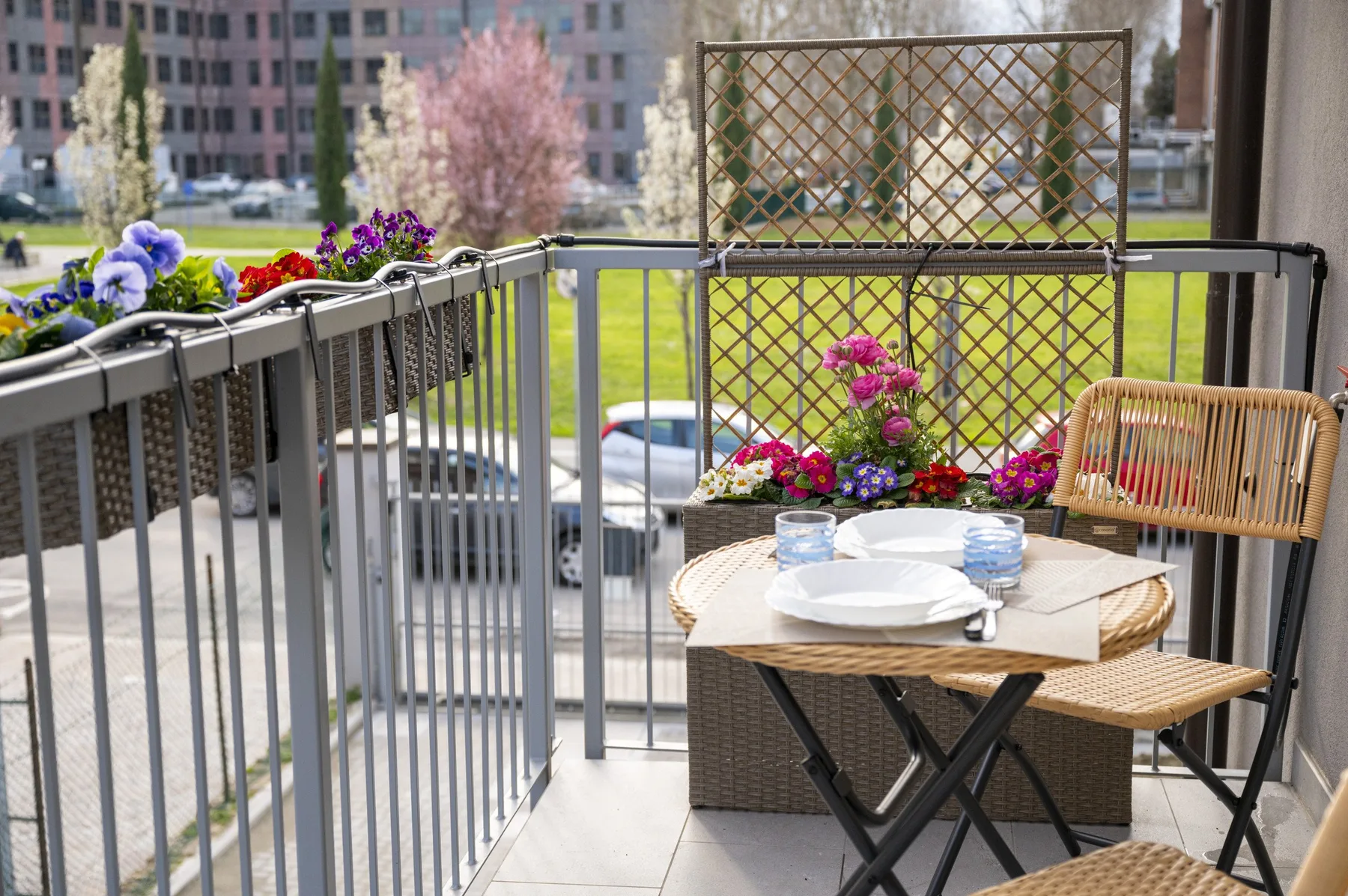 Un espacio de estar en un balcón con una mesa redonda, sillas y jardineras con flores.