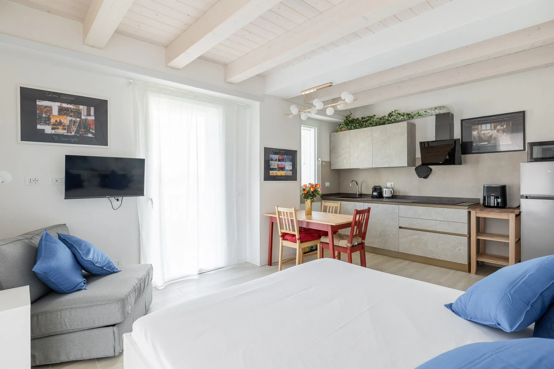 Un dormitorio luminoso con cocina pequeña, cama, asientos y mesa de comedor.