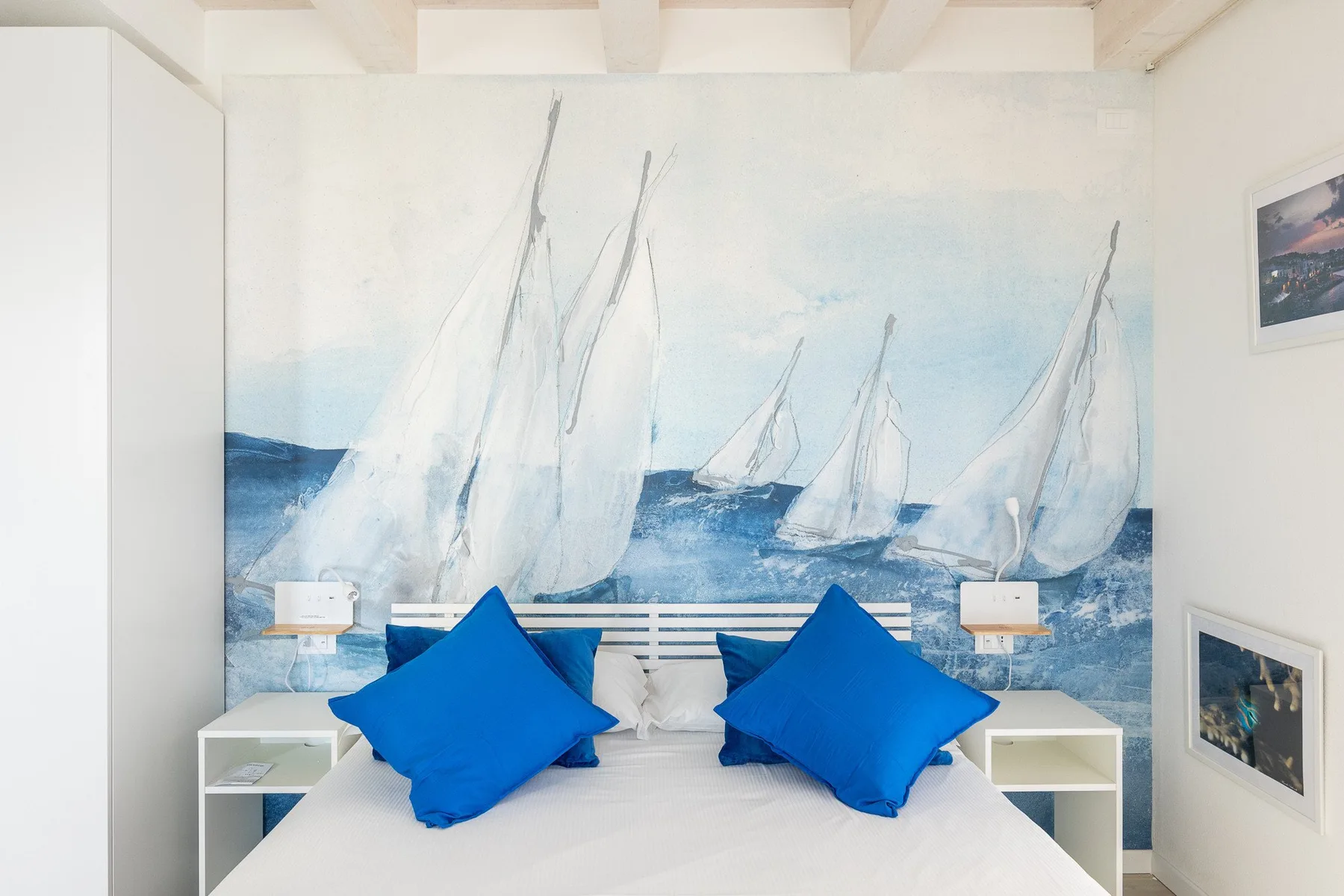 Un dormitorio con una cama frente a un mural de veleros en el mar.