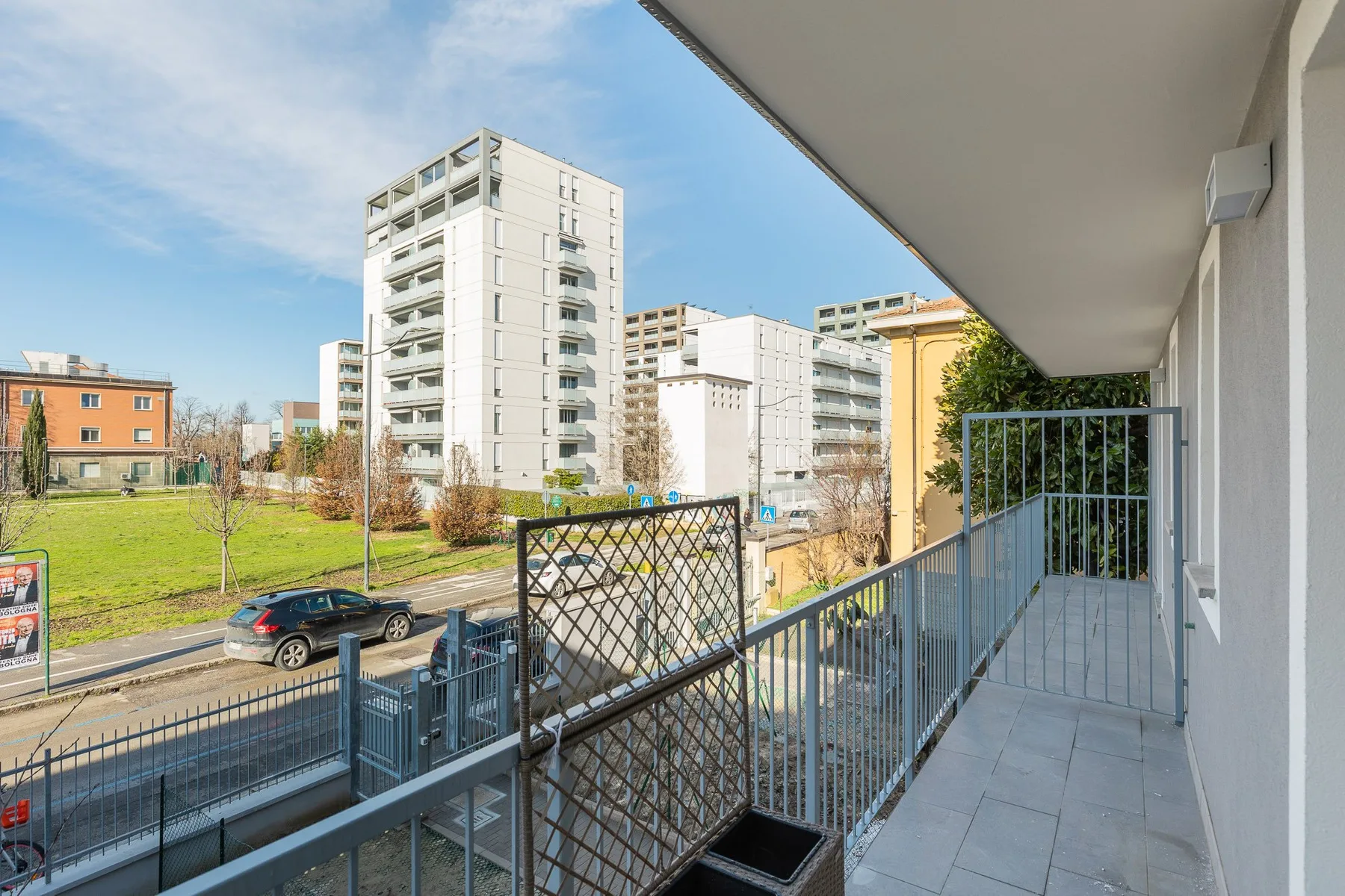 Un balcón da a una calle, una zona verde y edificios de apartamentos cercanos.