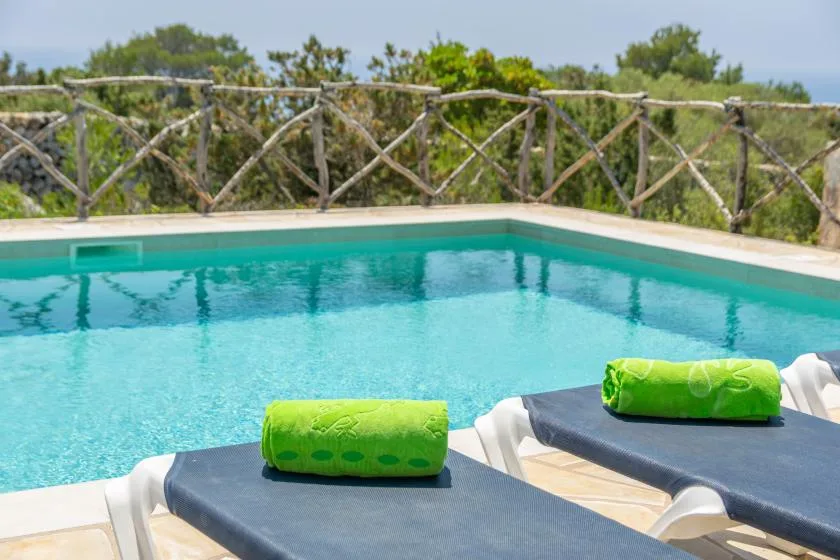 Una piscina al aire libre junto a tumbonas con toallas verdes.