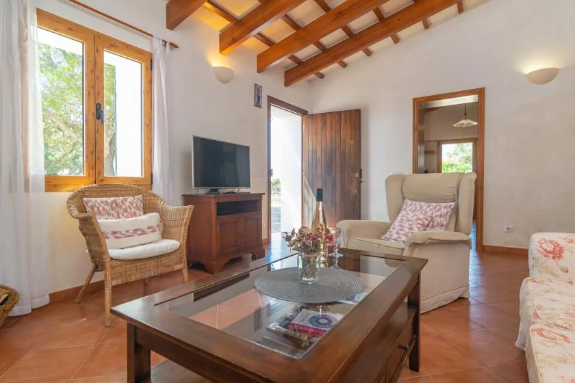Una sala de estar con asientos, un televisor y vigas de madera vistas en el techo.