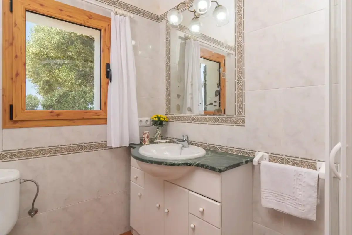 Un lavabo de baño con espejo está junto a una ventana.
