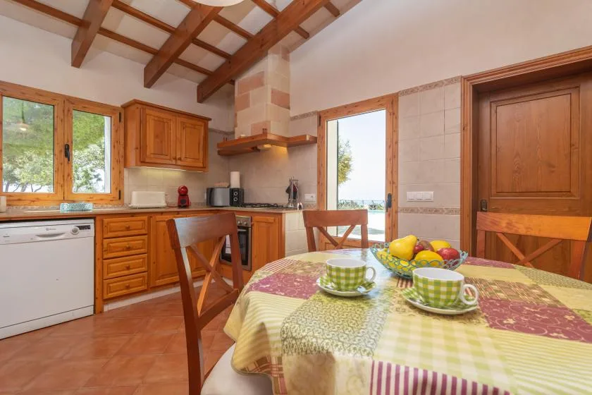 Cocina y comedor con muebles de madera y una mesa puesta con tazas y fruta.