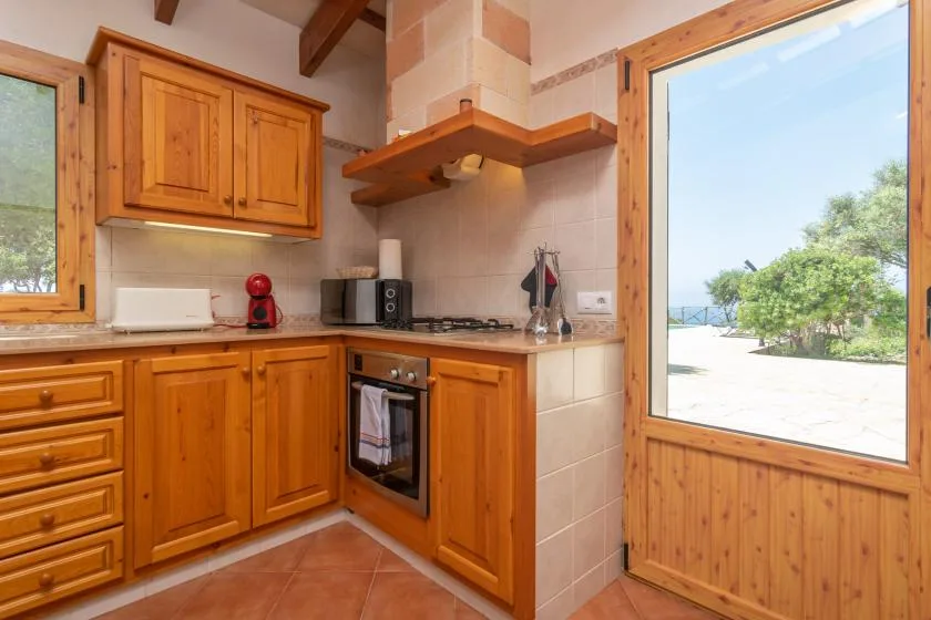 Una cocina de tonos cálidos con armarios de madera y una ventana amplia con vistas a la vegetación.
