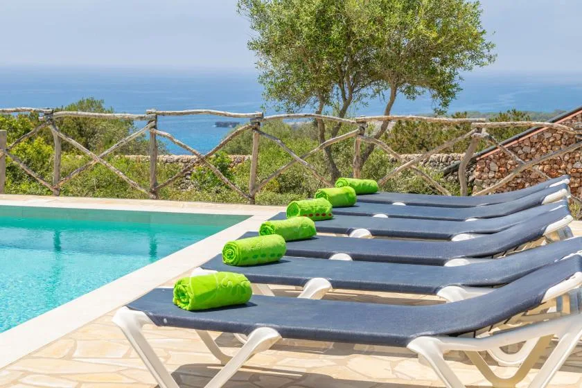 Una zona de descanso junto a la piscina mira al mar, con tumbonas junto al agua.