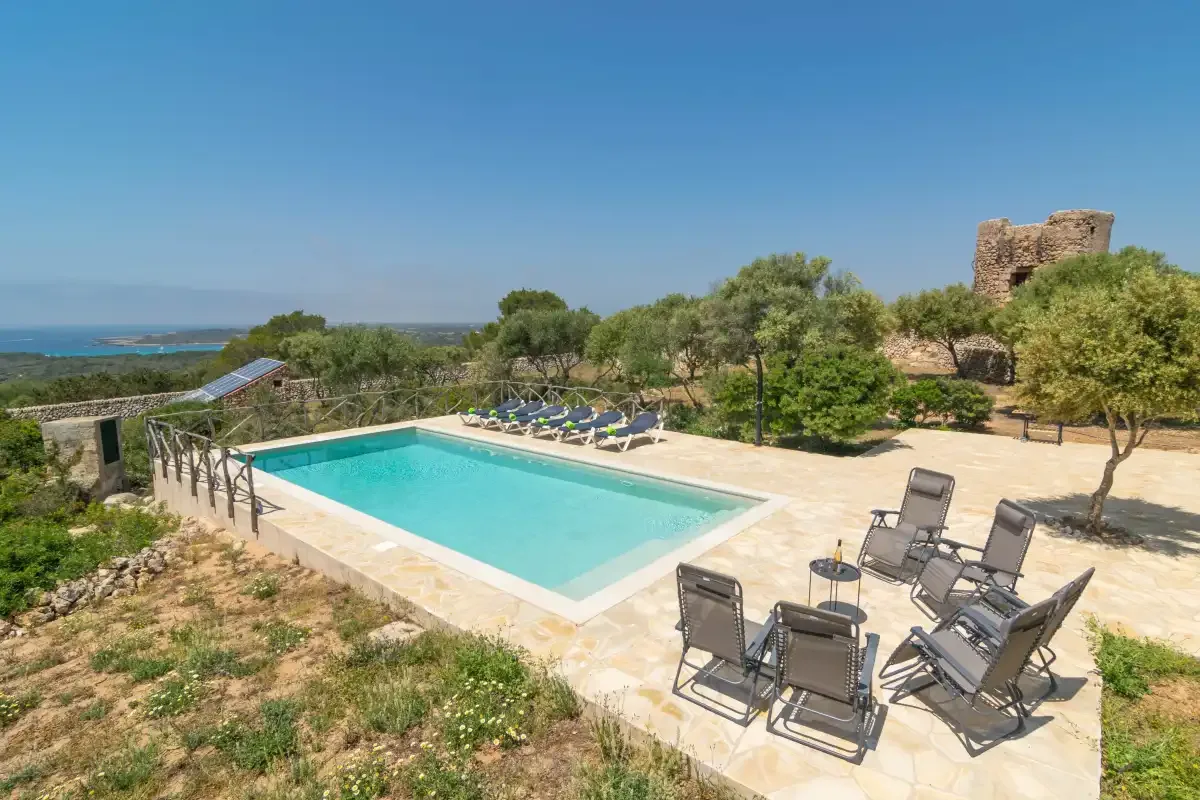 Una piscina al aire libre está rodeada por una terraza pavimentada y asientos reclinables.
