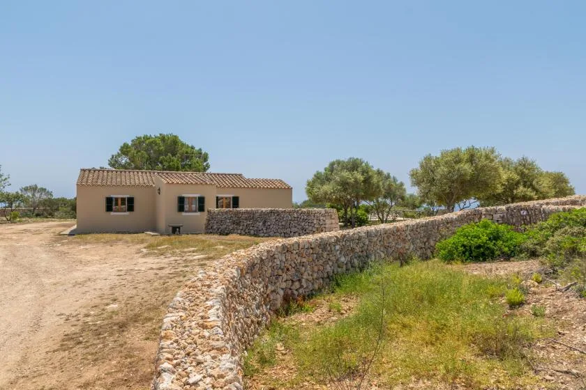 Un muro bajo de piedra bordea una casa pequeña en un paisaje seco y abierto.