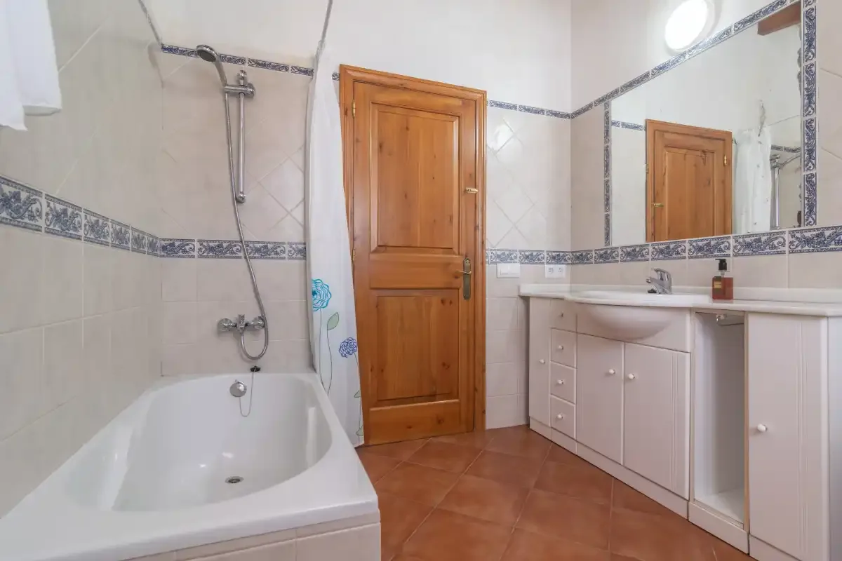 Baño con azulejos, bañera, puerta de madera y lavabo con mueble.