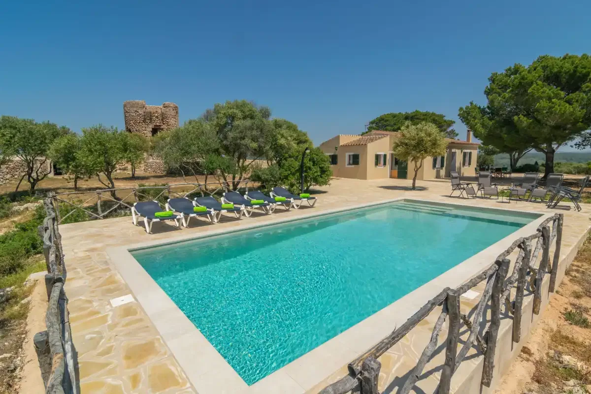 Una piscina al aire libre junto a un patio pavimentado y asientos de descanso.