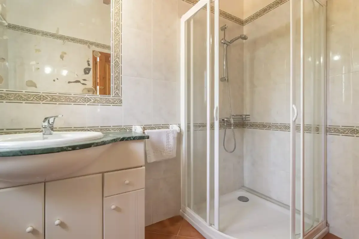 Baño con lavabo sobre un mueble y ducha con mampara de vidrio.