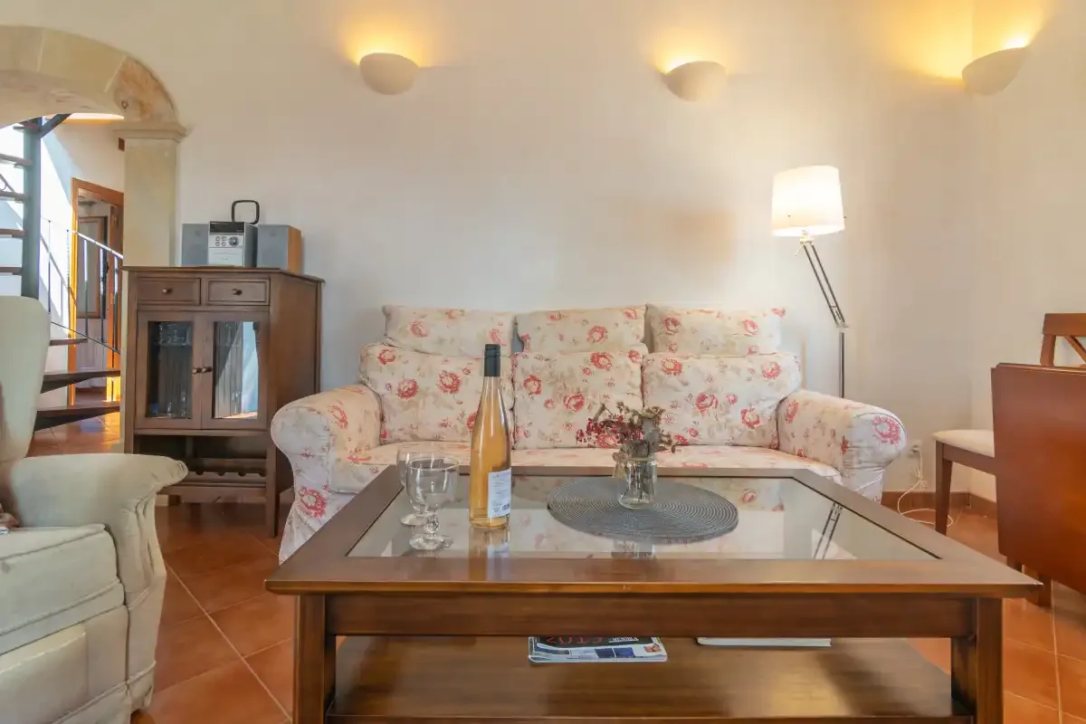 Una sala de estar con asientos florales y una mesa de centro con tapa de vidrio.