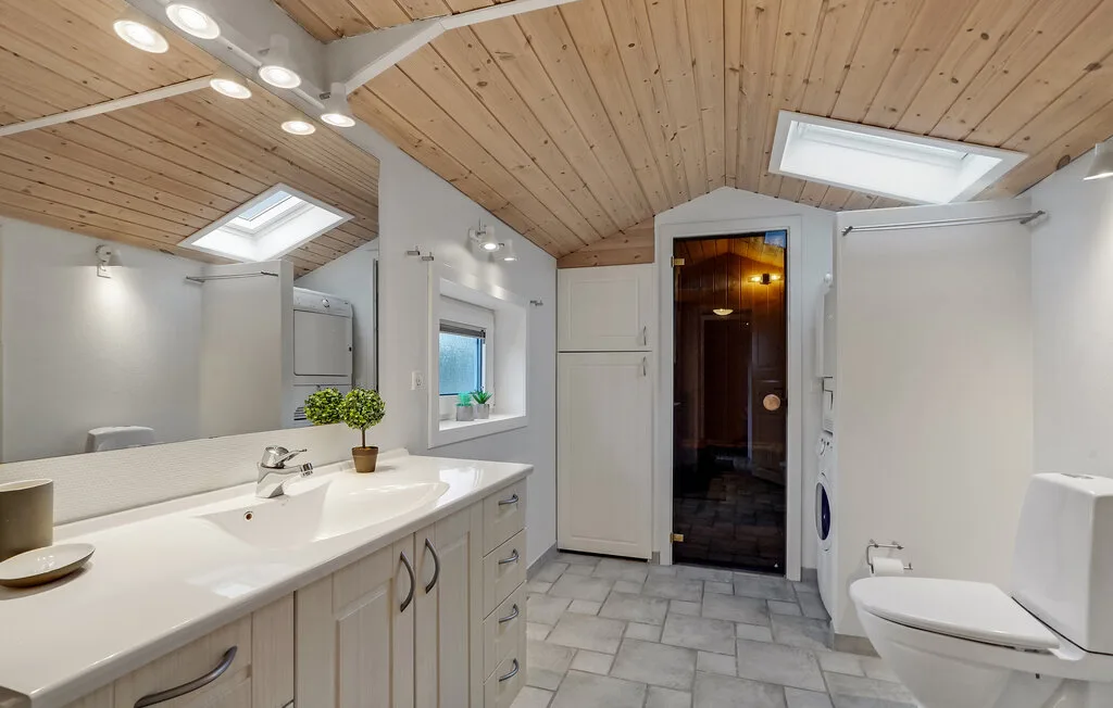 Un baño luminoso tiene un tocador largo, suelo de baldosas y una ducha de vidrio.