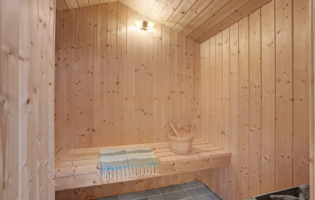 Una sauna revestida de madera con un banco elevado y un cubo pequeño.