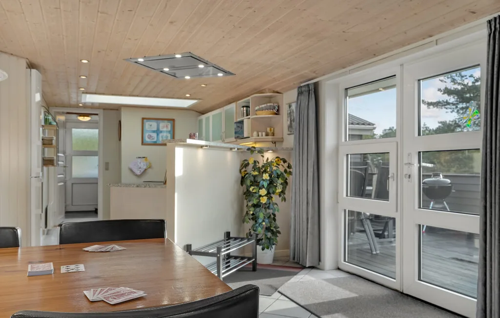 Una estancia diáfana y luminosa tiene una mesa de comedor, una cocina pequeña y ventanas amplias.