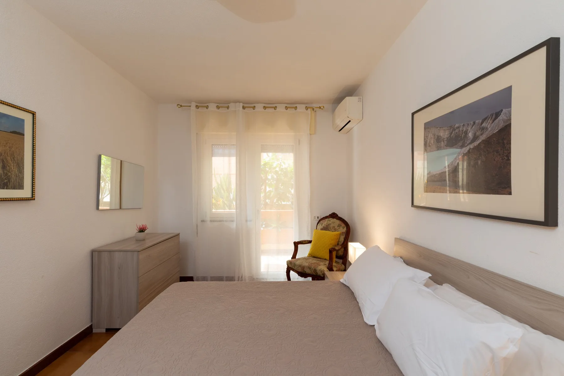 Un dormitorio luminoso con una cama, una cómoda y una puerta de cristal con cortinas.